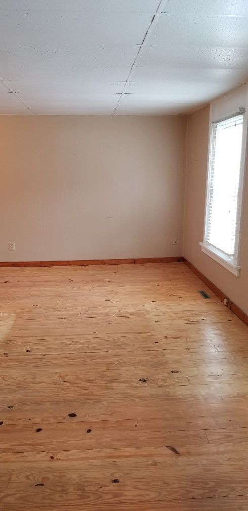 Empty room with light-colored walls and wood floors. A window is in the right corner.