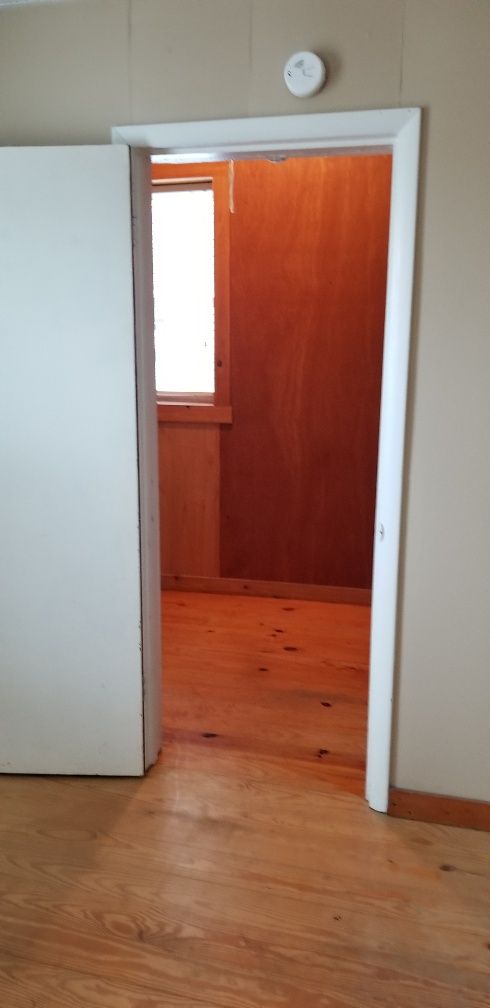 Ajar door opening to a small room with wood walls and flooring, and a window.