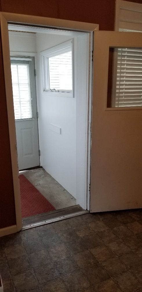 Interior doorway leading to a small hallway with a window, white door, and red rug. Brown flooring.