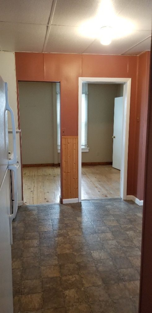 Interior view of a kitchen with two doorways to other rooms. Brown walls, a linoleum floor, and a white refrigerator are visible.