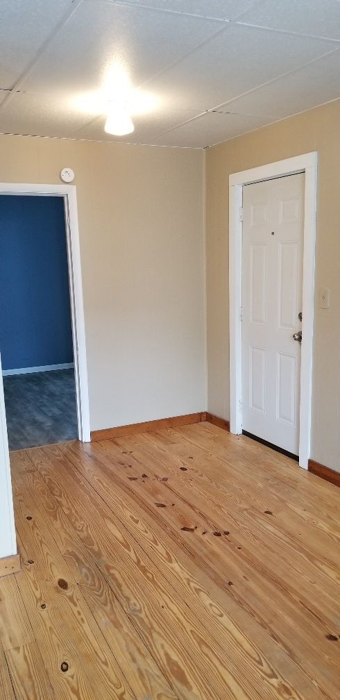 Empty room with wooden floors, tan walls, white door, and doorway to a blue room.