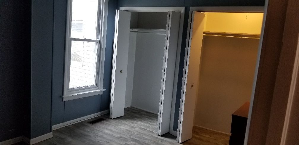 Bedroom interior with two closets and a window. Blue walls, gray floor, white trim.