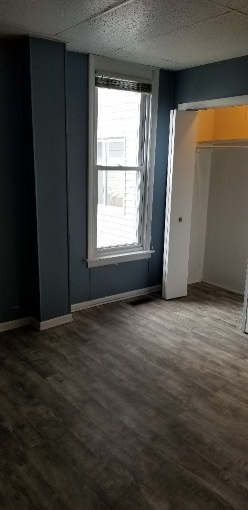 Empty room with blue walls, a window, and wood-look flooring. A closet is on the right.