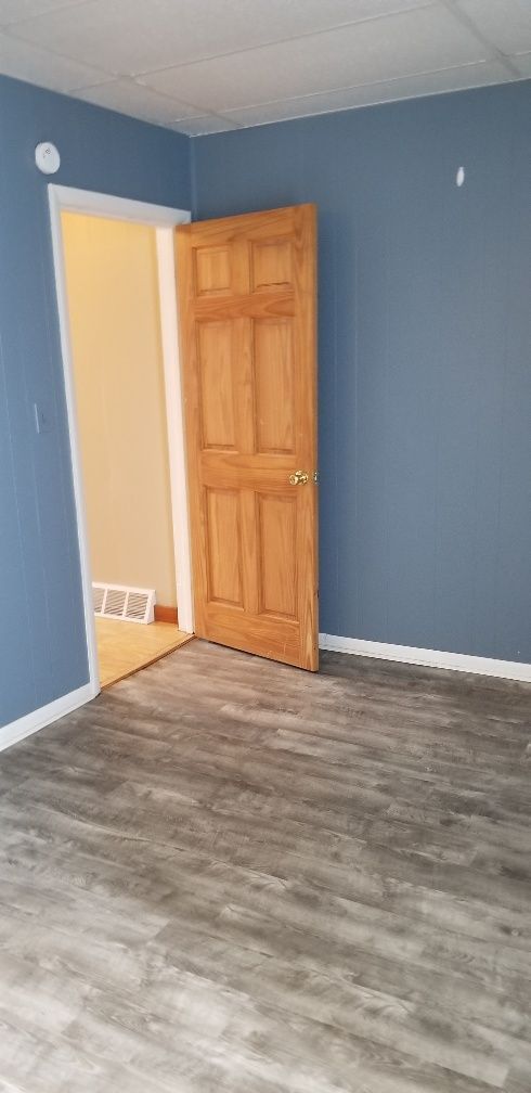 Empty room with wood door, blue walls, white trim, and gray flooring.