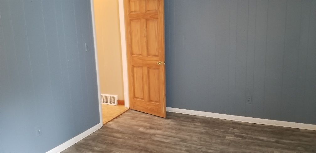 An empty room with blue walls, a wooden door, and wood-look flooring.