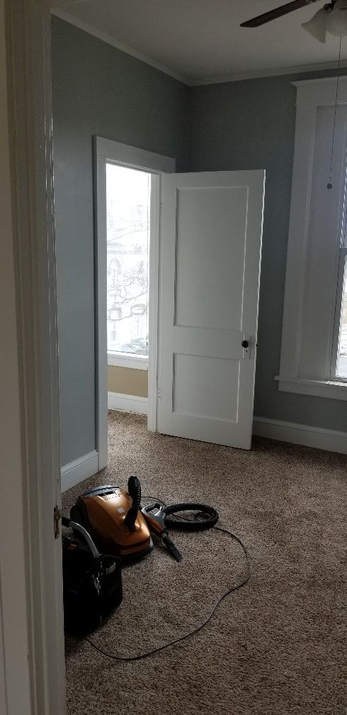 Room interior with open door, carpet, vacuum cleaner, and window. Blue walls and white trim.