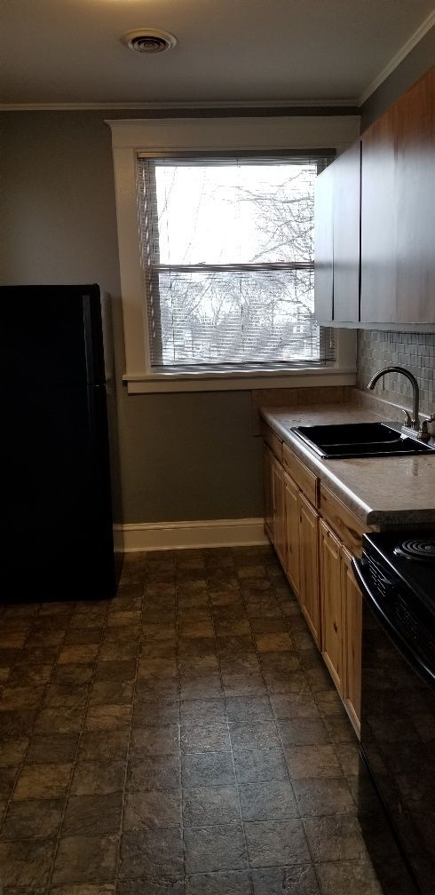 Kitchen with dark appliances, light cabinets, and a window. Brown tile flooring.