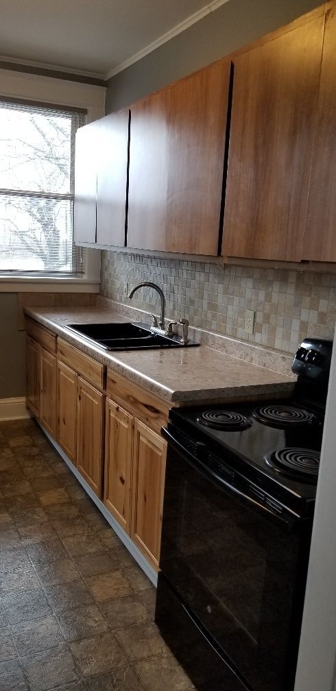 Kitchen with wooden cabinets, black stove, sink, and window.