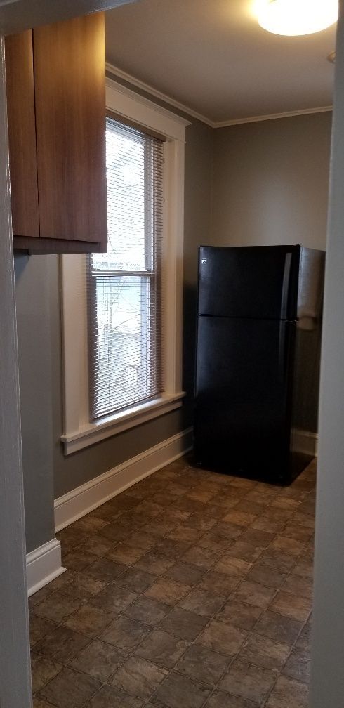 Small kitchen with black refrigerator, window, and brown tiled floor.