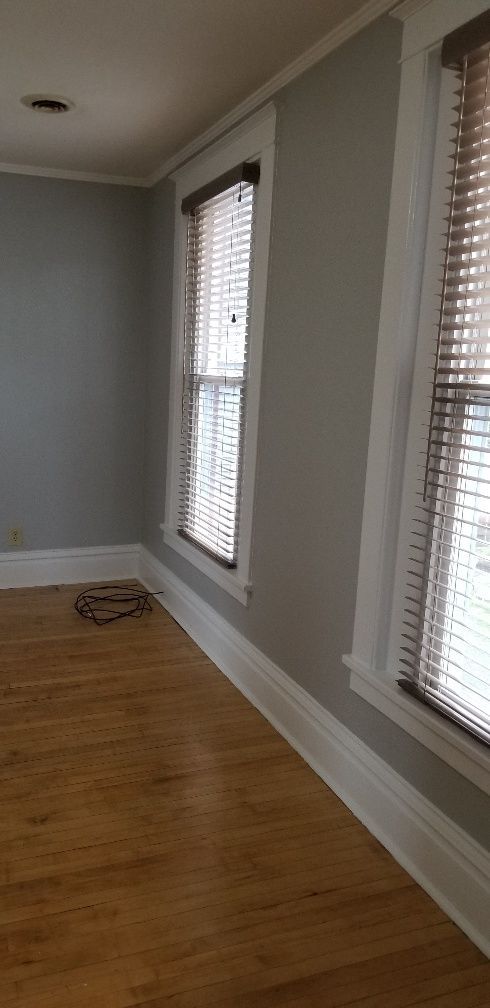 Interior view of a room with two windows, wood blinds, light grey walls, and hardwood floors.