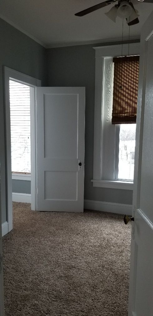 Bedroom interior with open door, window, brown carpet, white trim and ceiling fan.