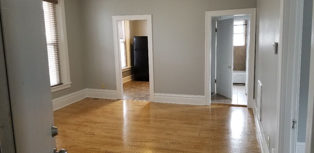 Empty room with hardwood floors, light gray walls, and open doorways to other rooms.