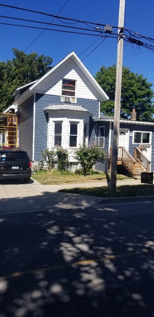 Blue house with white trim, porch, and a wooden staircase.  Black car parked on street in front.