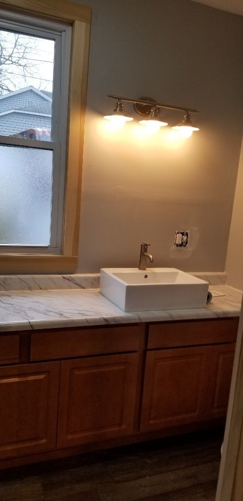 Bathroom with a white square sink on a marble countertop above brown cabinets, a window on the left.