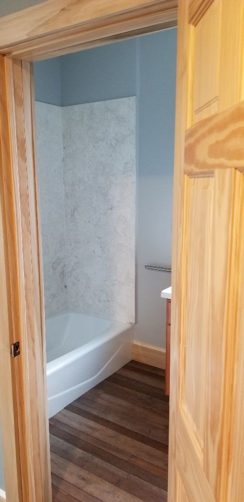 View into a bathroom with a bathtub, wood floor, and blue walls, through a doorway.