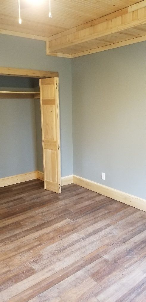 Empty bedroom with wood-look flooring, light blue walls, and wooden trim. Closet with bi-fold doors.