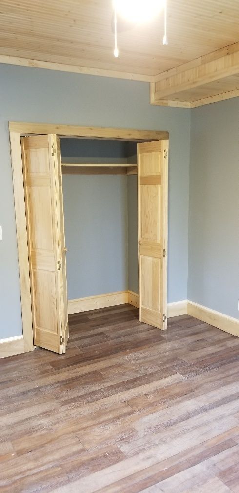 Empty bedroom with open closet doors, wood flooring, and blue walls.