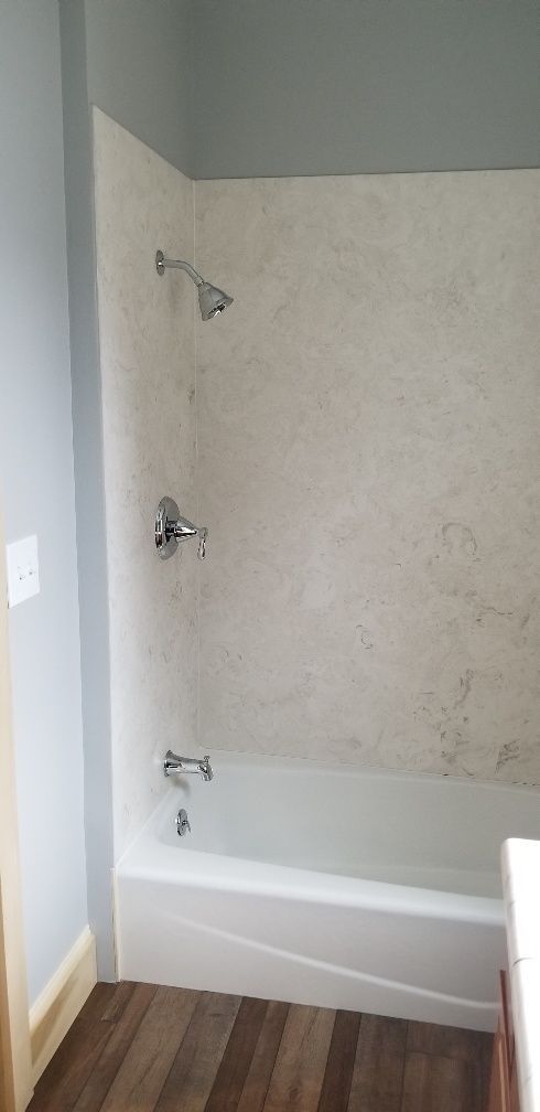 A white bathtub and shower with fixtures against a textured beige wall, wooden floor, and blue paint.