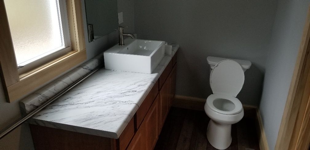 Bathroom with white sink, toilet, and wooden cabinetry. The walls are gray, and the floor is wood-like.
