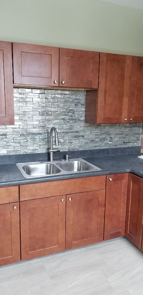 Kitchen with brown cabinets, gray backsplash, and stainless steel double sink.