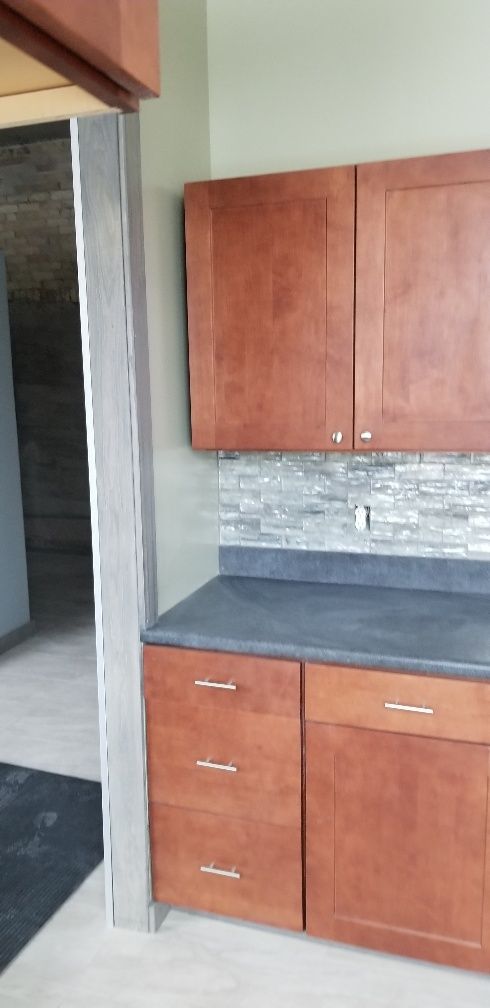 Kitchen cabinets and countertop in a room. Brown cabinets, dark countertop, and tiled backsplash.
