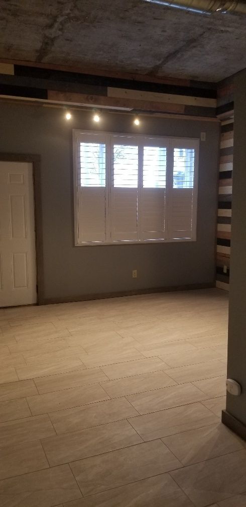 Empty room with window, wood floors, and exposed ceiling. Gray walls and natural light.