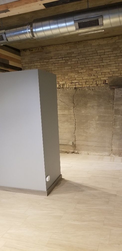 Gray wall in a room with a concrete wall and wooden floor. There is ductwork above.