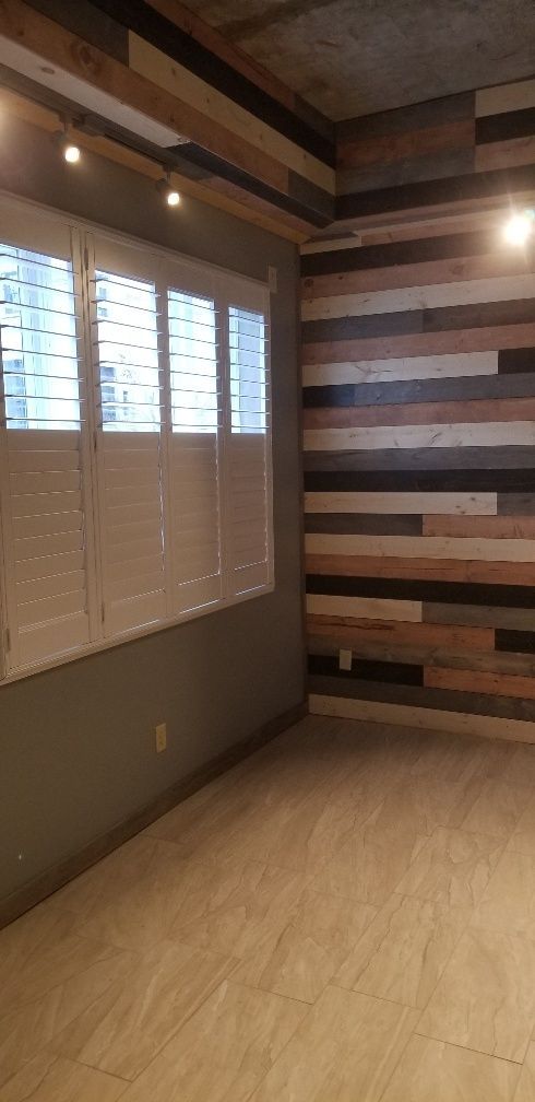 An empty room with wood paneling on the ceiling and a wall, a window with blinds, and light-colored flooring.