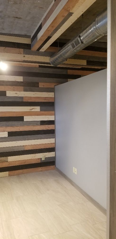 Room with wood paneling on the wall and ceiling, light gray wall, and light wood flooring.