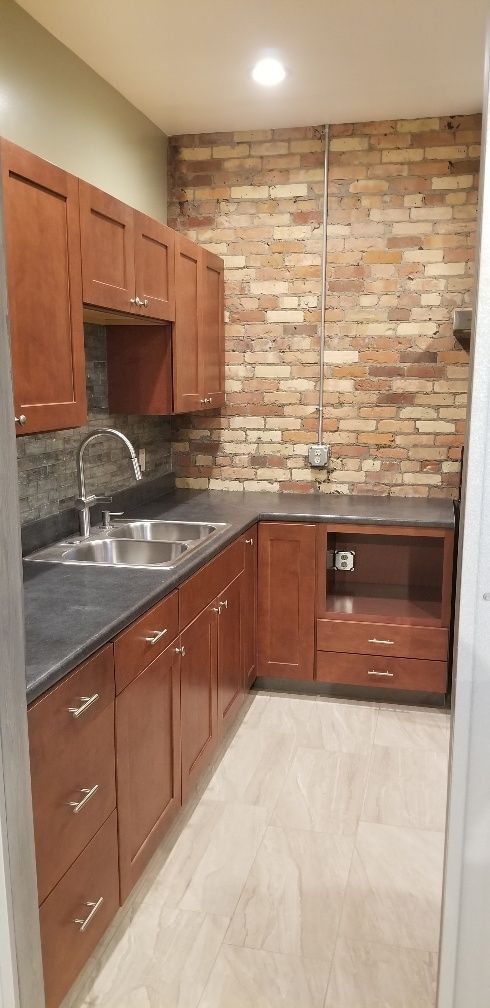 Kitchen with wooden cabinets, stainless steel sink, brick backsplash, and light-colored floor.