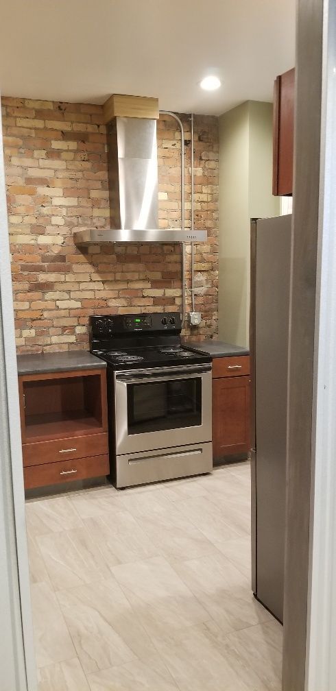 Kitchen with exposed brick wall, stainless steel appliances, and wooden cabinets.