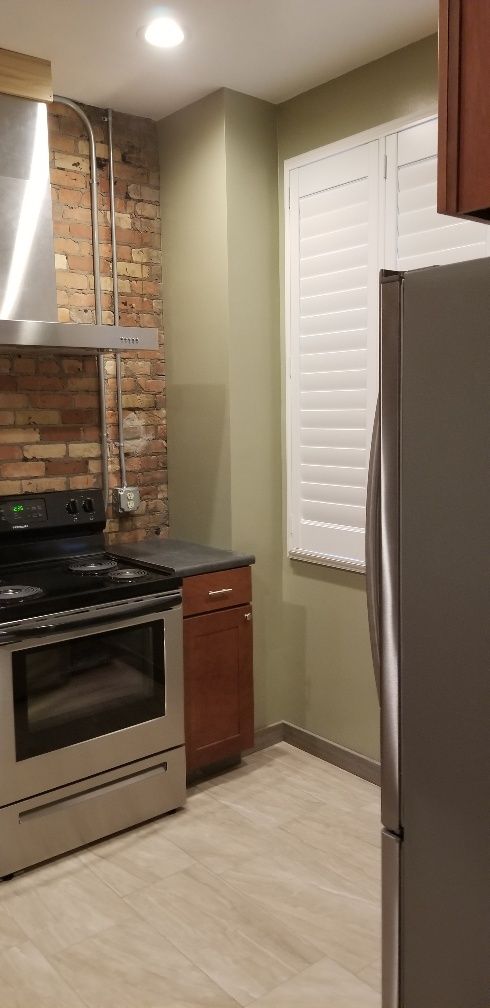 Kitchen with brick backsplash, stainless steel appliances, and shutters. Light wood-look flooring.