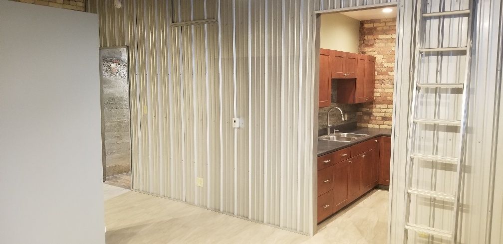 Interior with metal walls and a glimpse of a kitchen with brick wall and wooden cabinets.
