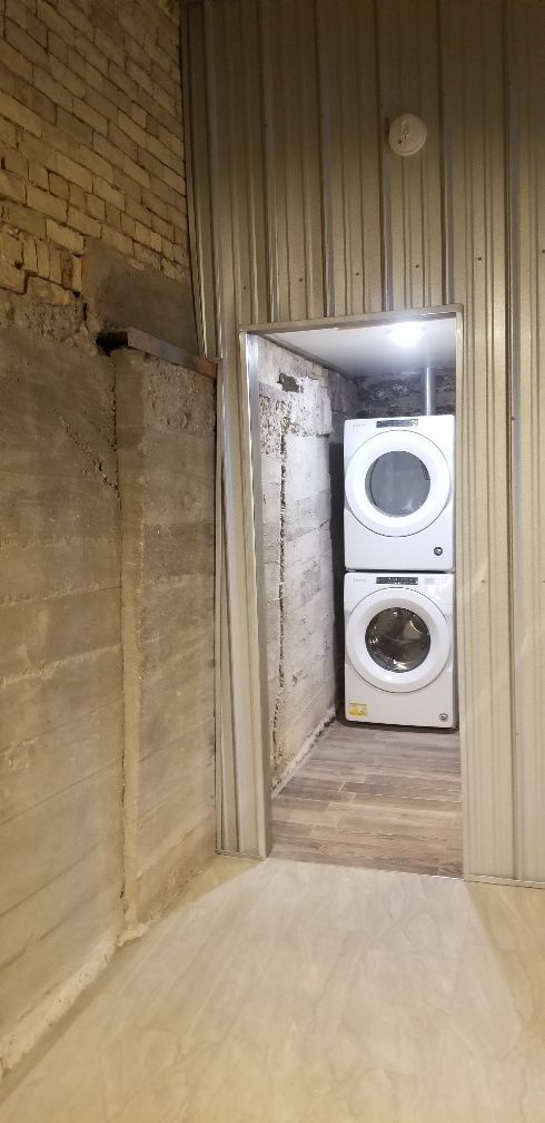 Stacked washer and dryer in a small laundry room framed by metal and concrete walls.
