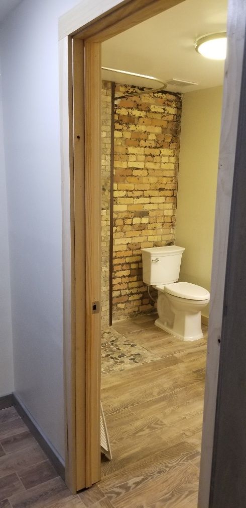A doorway opens to a bathroom with brick wall and toilet. Light-colored wooden floor.