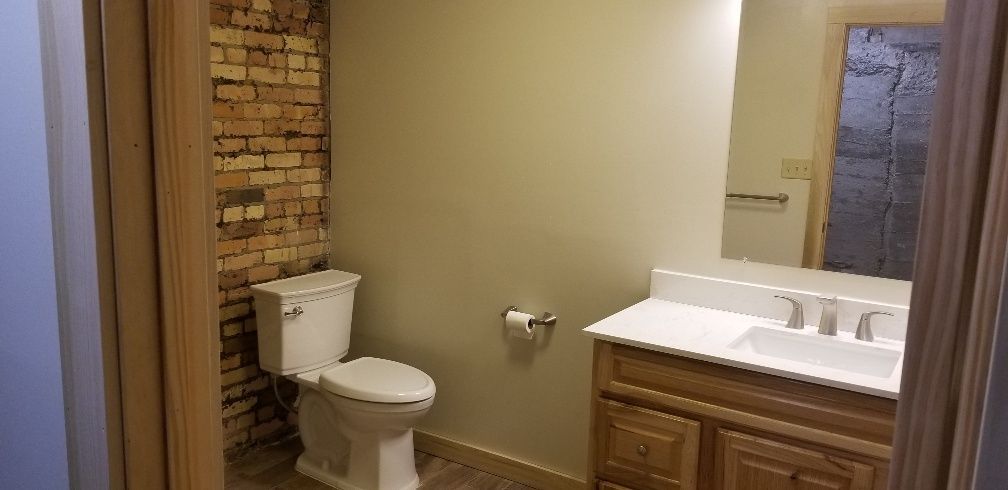 Bathroom with exposed brick accent wall, toilet, sink with mirror, and wooden vanity.