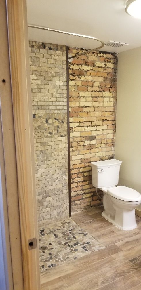 Bathroom with exposed brick wall, toilet, and shower with stone tile floor. Wooden floor.