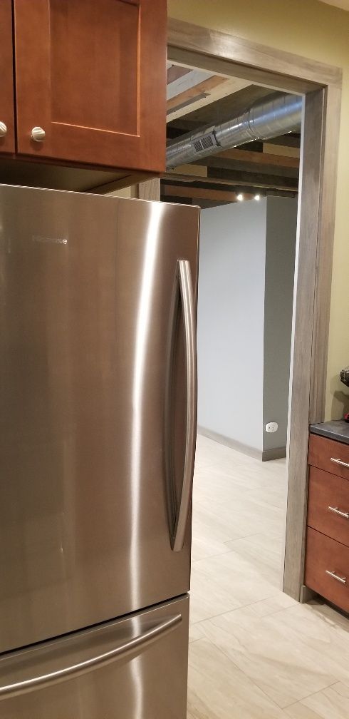 Stainless steel refrigerator beside open doorway into room with pale gray walls.