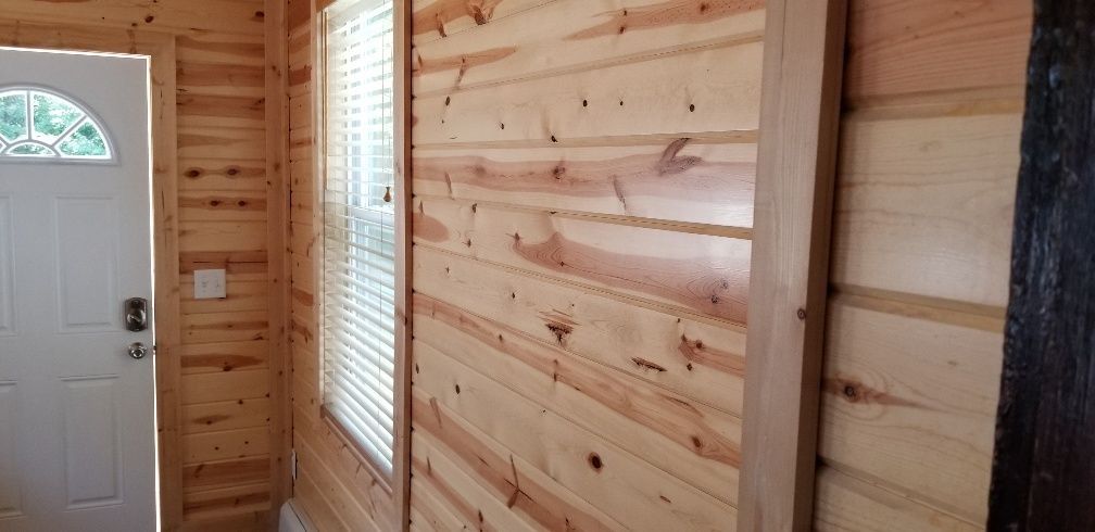 Interior of a room with wood paneling, a window with blinds, and a white door with a decorative window.