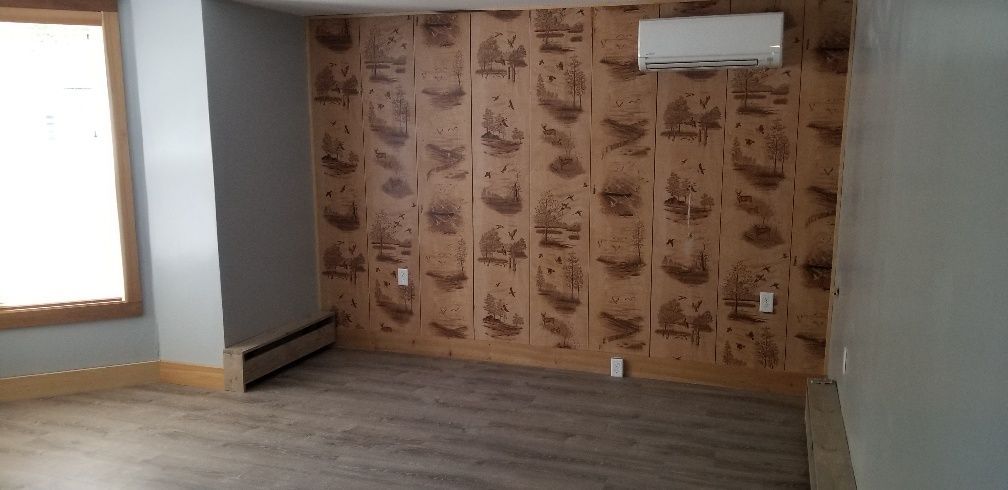 Empty room with patterned wood wall, window, air conditioner, and gray floors.