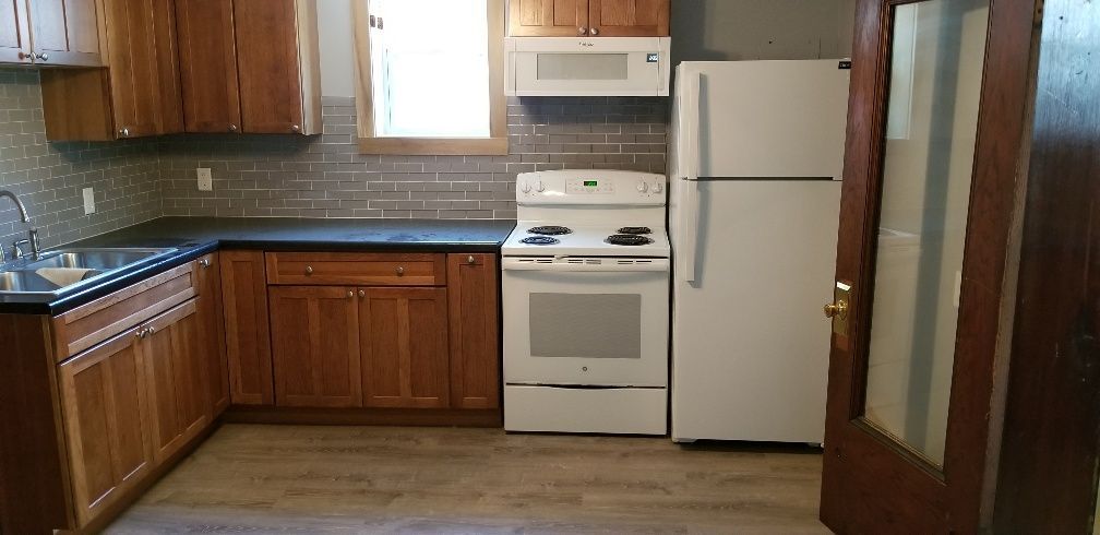 A kitchen with wooden cabinets, a white stove, and a refrigerator. There is a window and a door.