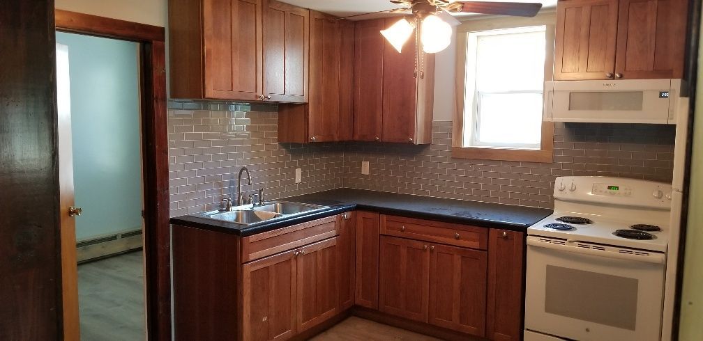 A kitchen with brown cabinets, black countertops, and a white stove. A doorway is to the left.