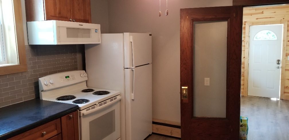 Kitchen with a stove, refrigerator, cabinets, and a doorway leading to another room.