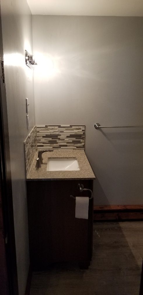 A small bathroom with a sink, mirror, and towel rack. The walls are gray, and the floor is a dark wood.