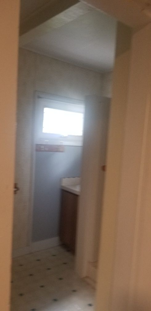 Bathroom interior, seen through a doorway. Features a window, vanity, patterned floor, and pale walls.