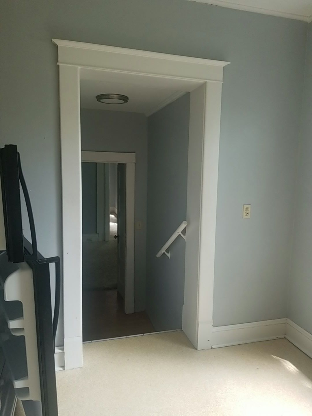 Open doorway with white trim, leading to hallway with stairs. Blue walls, beige carpet.