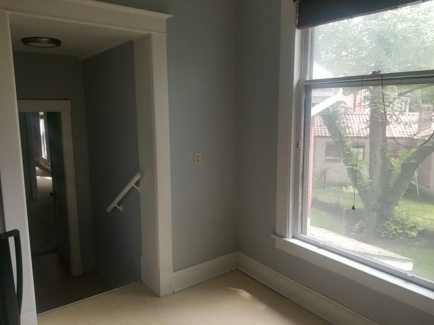 Room with a window and a doorway, gray walls, white trim, and a glimpse of the outdoors.