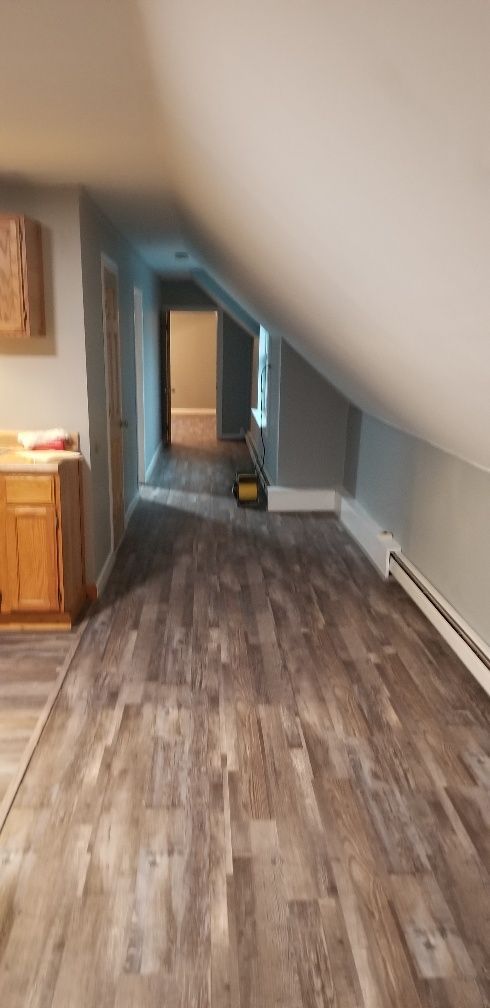 Attic room with wooden floor, sloped ceiling. Doorways on the left and ahead. A window on the right.