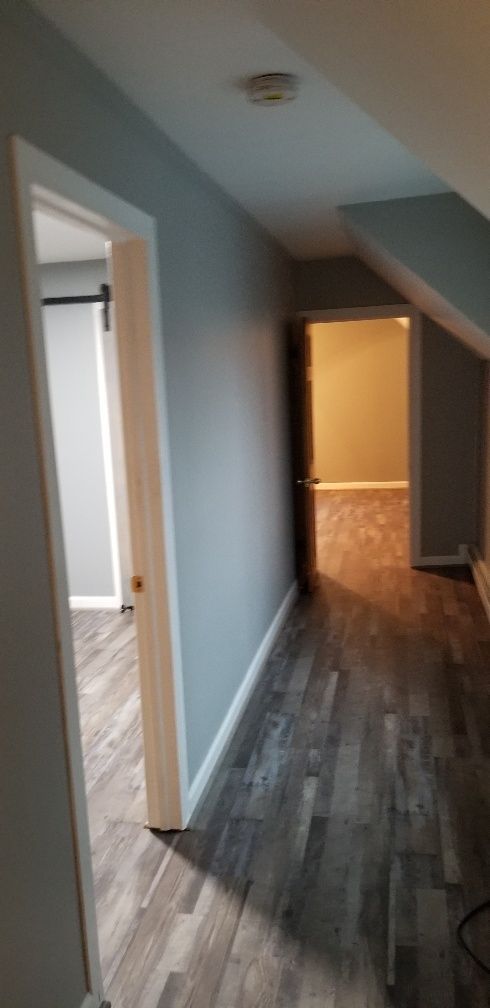 Hallway with gray-blue walls and wood-look flooring. Two open doors lead to rooms.