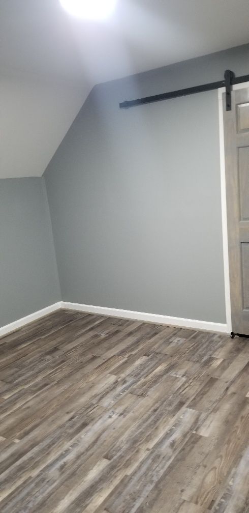 A room with gray walls and wood-look flooring. A sliding door and sloped ceiling are visible.